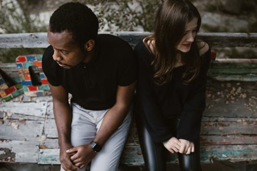 A couple sitting apart on a park bench, expressing emotions. Outdoors setting.