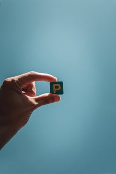 A hand holds a Scrabble tile with the letter 'P' against a blue sky, symbolizing creativity and communication.