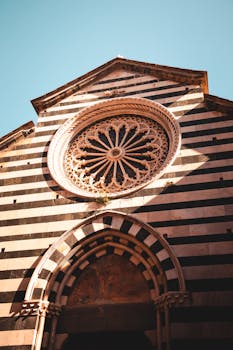 Ornate facade of a classic Italian church with striped design and intricate rose window in Liguria.