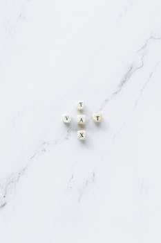 White dice spelling 'Tax' and 'VAT' on a marble surface, symbolizing taxation concepts.